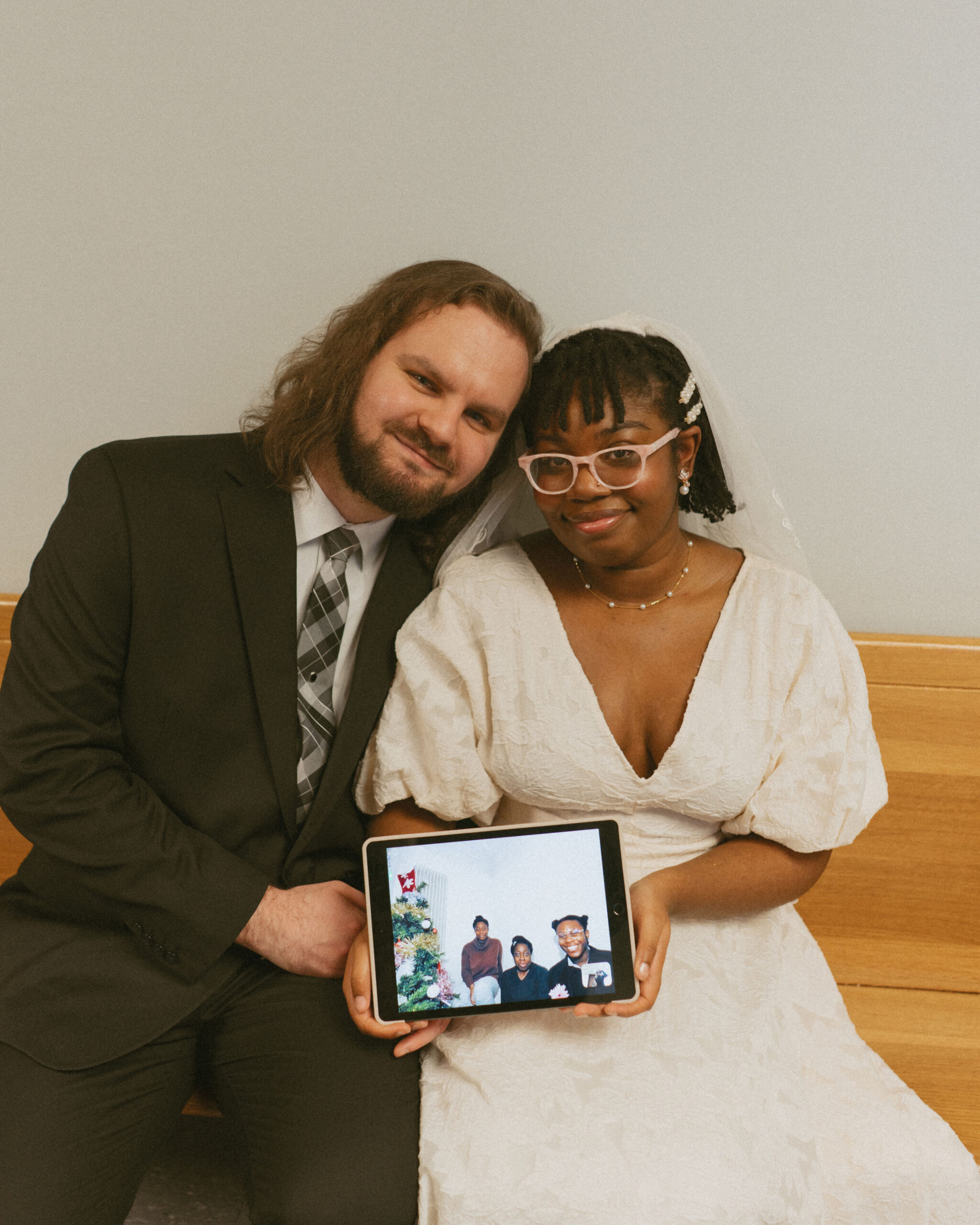 Bride and Groom in wedding attire sitting on courthouse bench holding an I pad while Facetiming family members during their elopement
