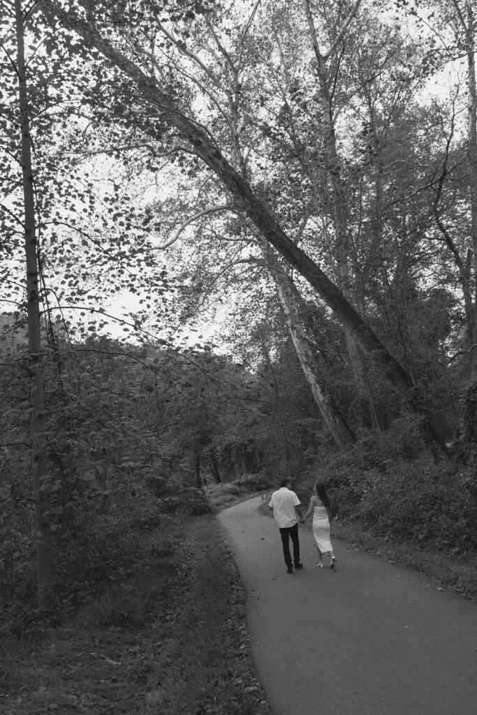 Engaged couple holding hands and walking down a path in park