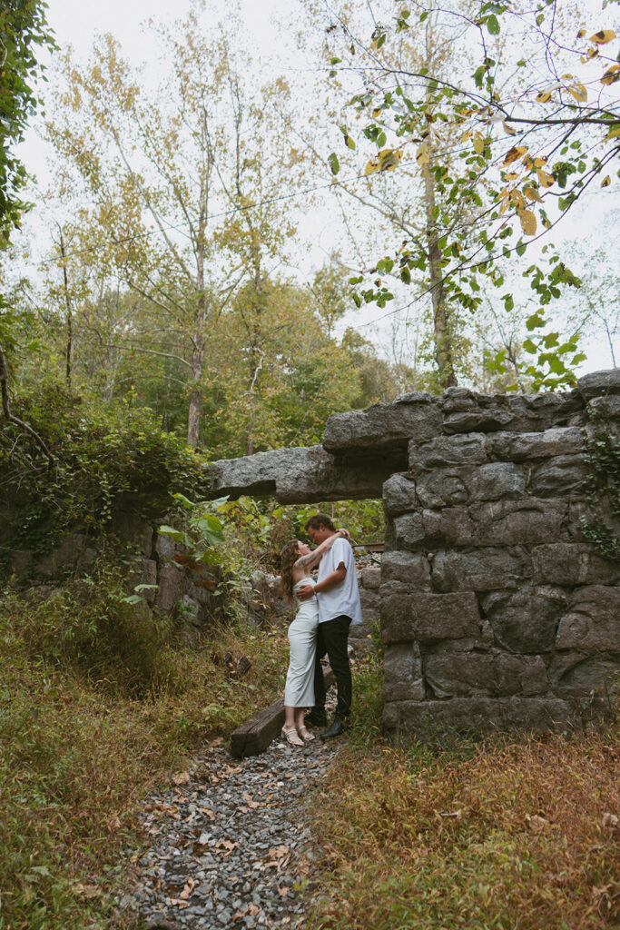 Engaged couple kissing in the woods next to a structure in a state park